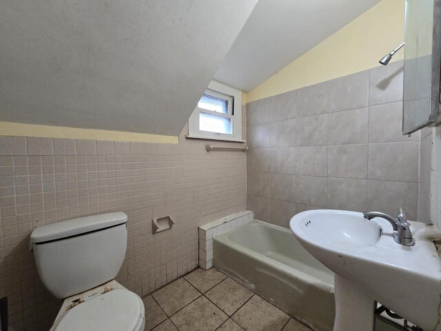 full bathroom with tile patterned flooring, vaulted ceiling, toilet, and tile walls