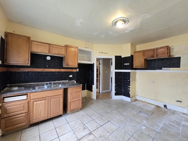 kitchen with light tile patterned flooring, dark countertops, brown cabinets, tasteful backsplash, and a sink
