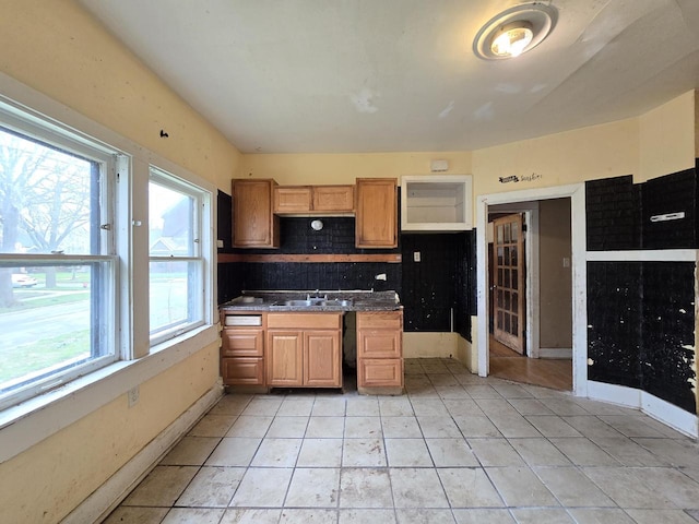 kitchen with a sink, dark countertops, baseboards, and backsplash