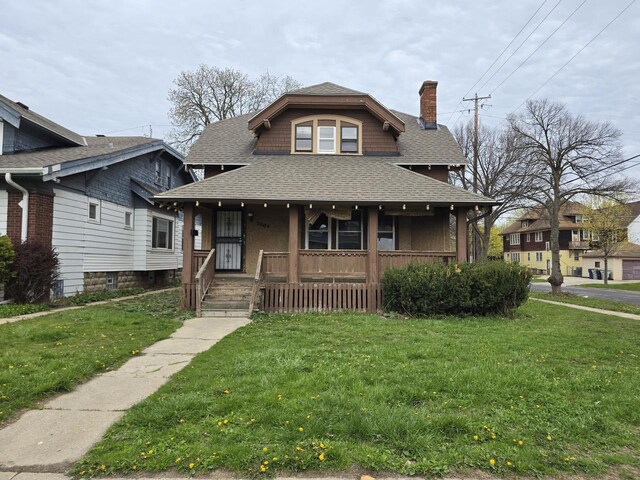 view of front facade featuring a shingled roof, a chimney, a porch, and a front lawn