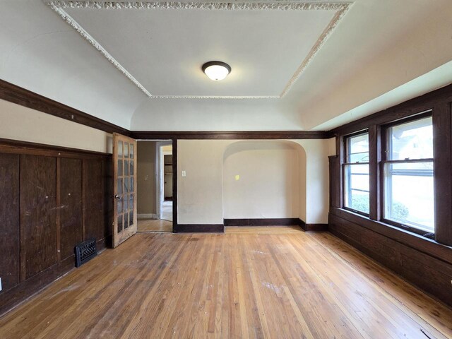 unfurnished room with arched walkways, vaulted ceiling, and light wood finished floors