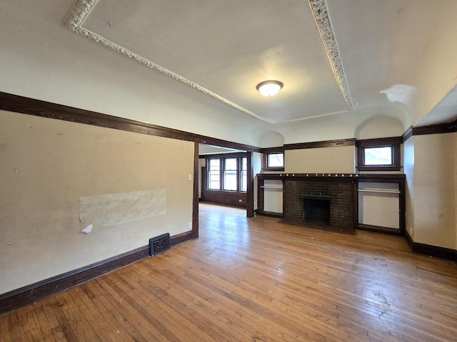 unfurnished living room with baseboards, wood-type flooring, a brick fireplace, and visible vents