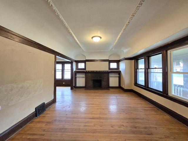 unfurnished living room with visible vents, baseboards, a brick fireplace, and hardwood / wood-style flooring