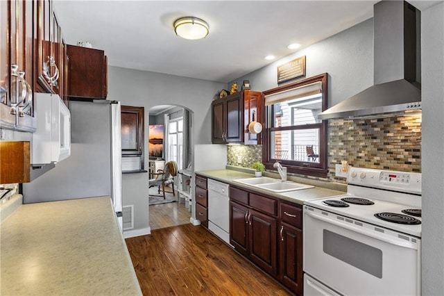 kitchen featuring wall chimney range hood, arched walkways, a sink, dark wood-style floors, and white appliances