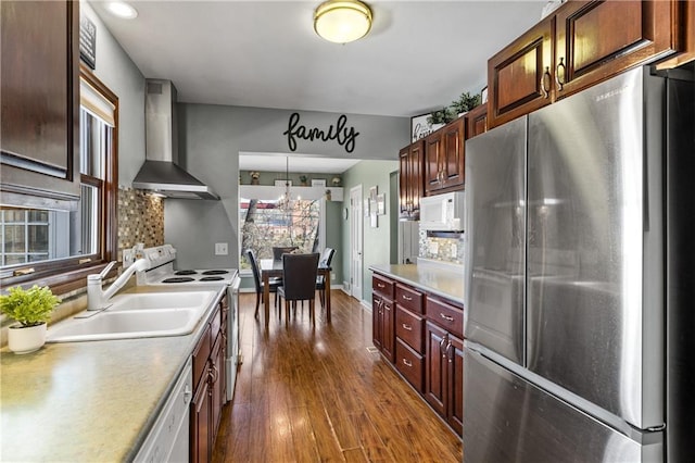 kitchen with a sink, white appliances, light countertops, dark wood finished floors, and wall chimney exhaust hood