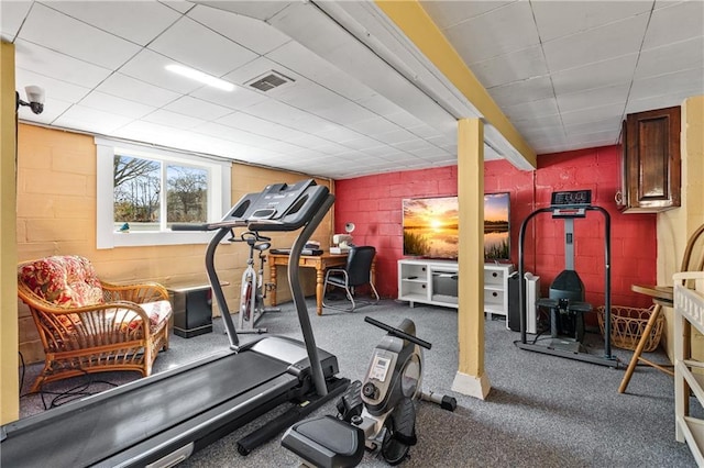 workout room with concrete block wall, visible vents, and a drop ceiling