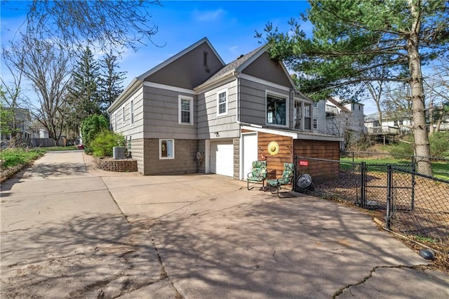 view of side of property featuring fence, central air condition unit, driveway, and a garage
