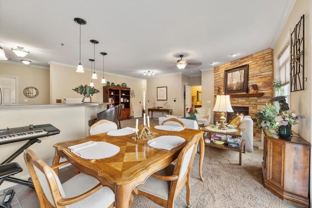 dining space with crown molding, a ceiling fan, light carpet, and a stone fireplace