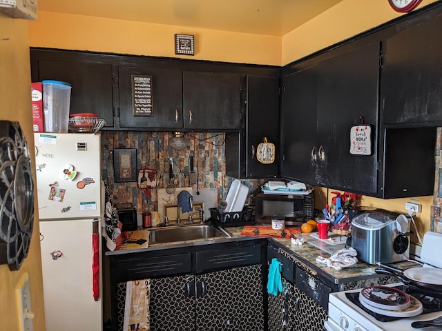 kitchen featuring dark cabinetry, a sink, and white appliances