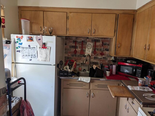 kitchen with brown cabinetry, range, black microwave, a sink, and freestanding refrigerator