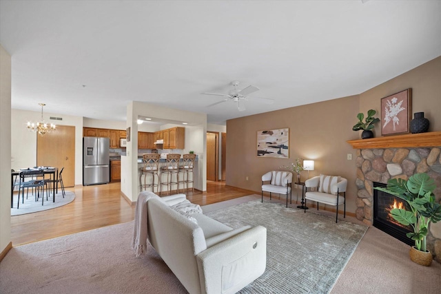 living area featuring visible vents, light carpet, a stone fireplace, light wood finished floors, and ceiling fan with notable chandelier