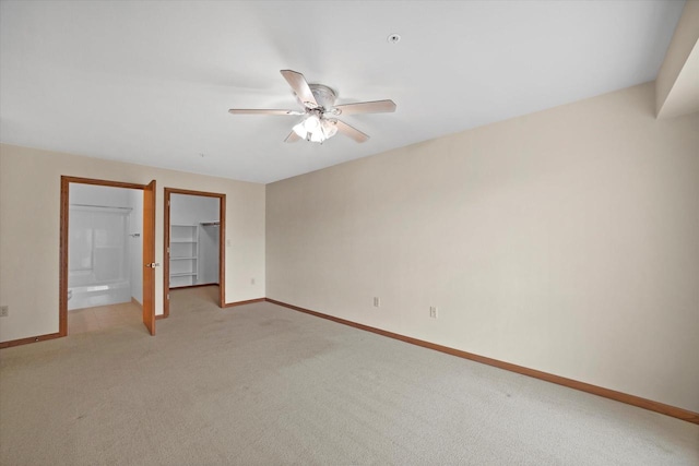 unfurnished bedroom featuring light colored carpet, a walk in closet, a ceiling fan, baseboards, and a closet