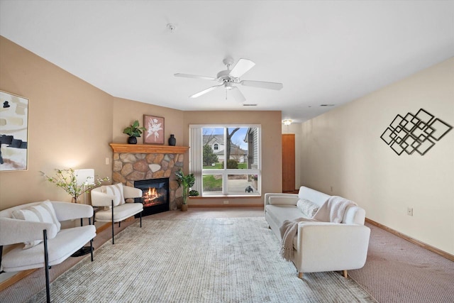 living area with baseboards, a stone fireplace, ceiling fan, and carpet