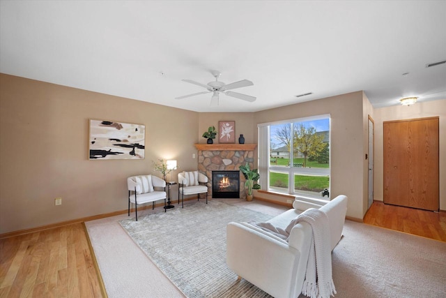 living room featuring ceiling fan, a stone fireplace, baseboards, and light wood-type flooring