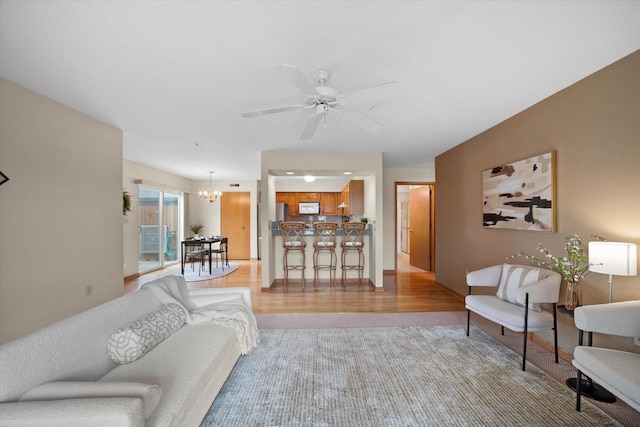 carpeted living area with baseboards and ceiling fan with notable chandelier