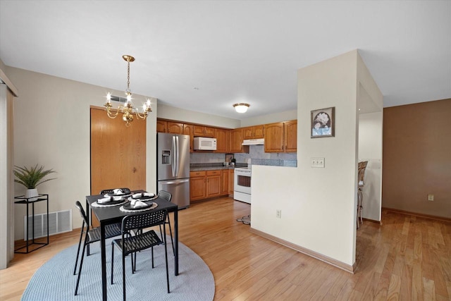 kitchen with an inviting chandelier, light wood-style floors, under cabinet range hood, and white appliances