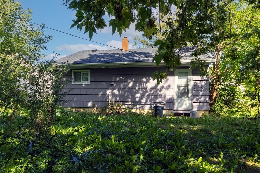view of home's exterior with roof with shingles and a chimney