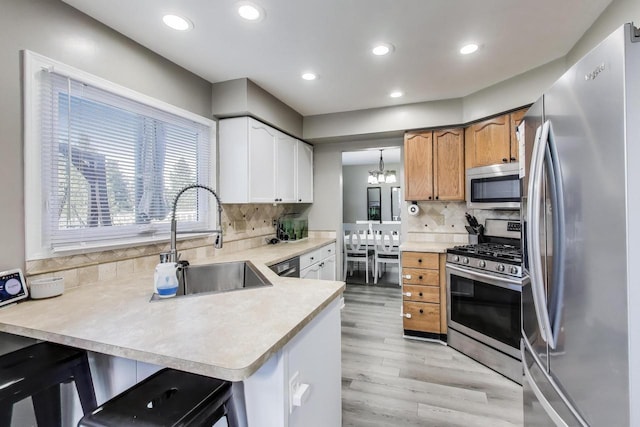 kitchen featuring a sink, light wood finished floors, light countertops, stainless steel appliances, and a peninsula