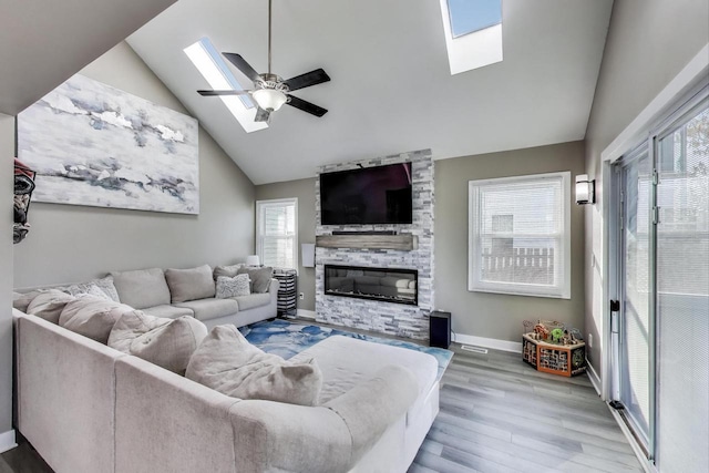 living area featuring baseboards, plenty of natural light, wood finished floors, and vaulted ceiling with skylight