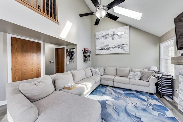 living area featuring a skylight, ceiling fan, wood finished floors, and high vaulted ceiling