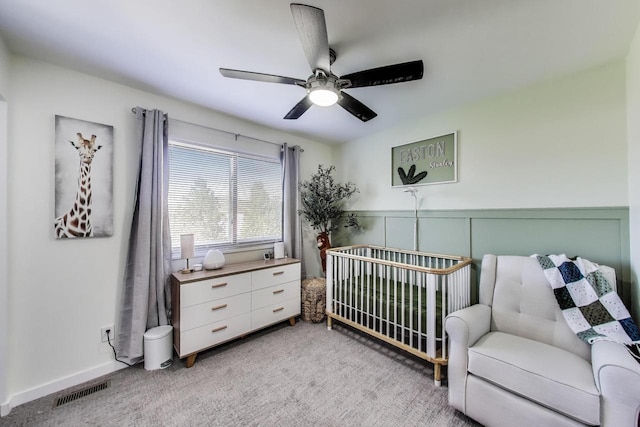 bedroom with a nursery area, visible vents, light carpet, and a wainscoted wall
