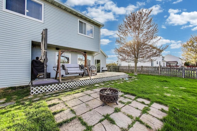 back of property with fence, a wooden deck, a yard, and a fire pit