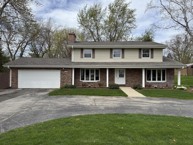 traditional-style house featuring driveway, a chimney, brick siding, an attached garage, and a front yard