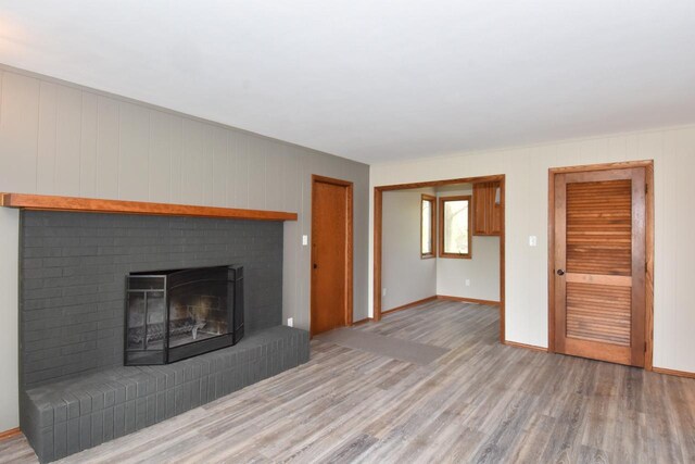 unfurnished living room featuring light wood-style flooring, a brick fireplace, and baseboards