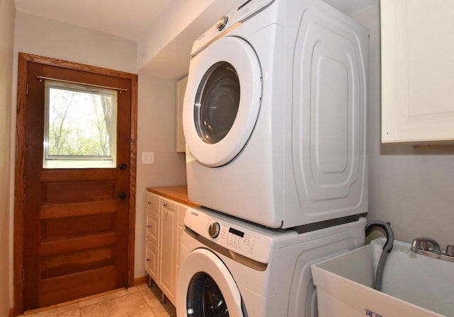 laundry room with cabinet space, stacked washer and clothes dryer, and light tile patterned flooring