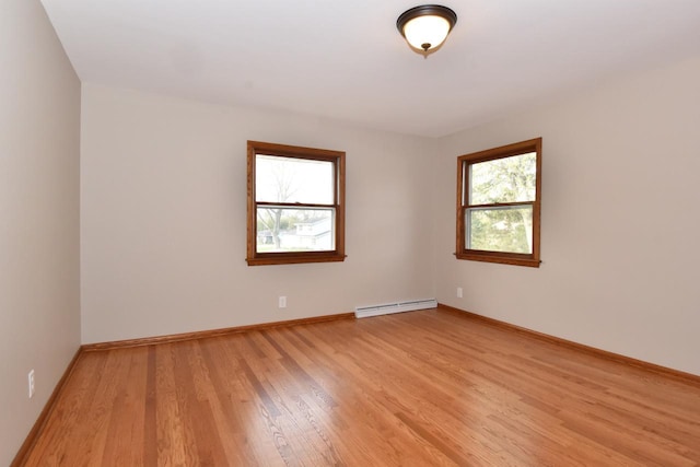 spare room with a baseboard radiator, light wood finished floors, and baseboards