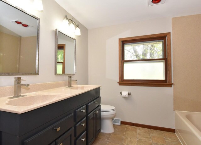 full bath with baseboards, toilet, a tub to relax in, and double vanity
