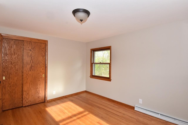 unfurnished bedroom with a baseboard heating unit, wood finished floors, and baseboards