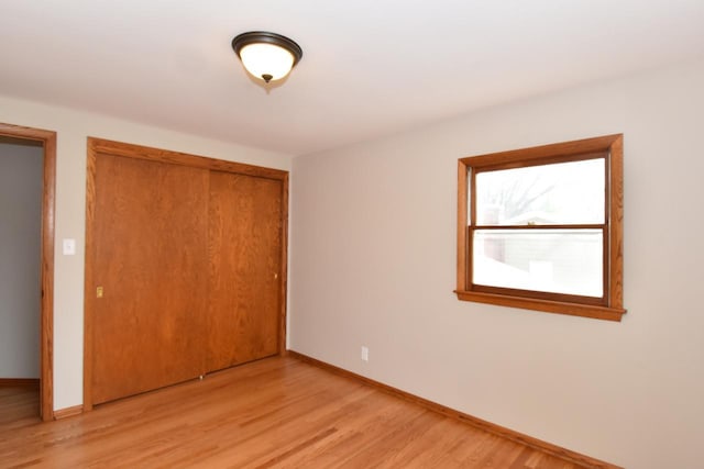 unfurnished bedroom with light wood-style flooring, baseboards, and a closet