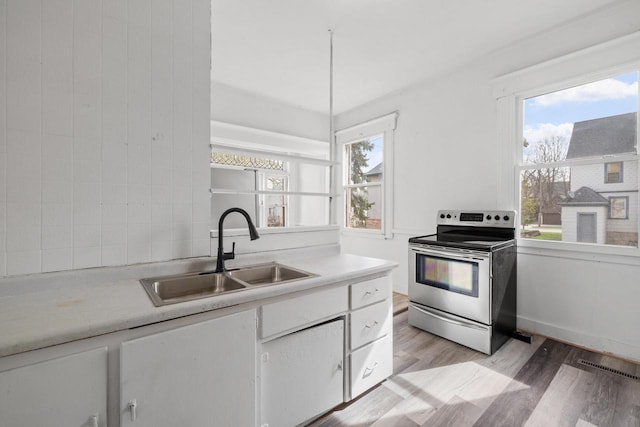 kitchen featuring backsplash, light countertops, a sink, white cabinets, and stainless steel electric stove
