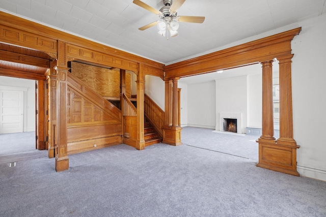 unfurnished living room with a ceiling fan, a fireplace with flush hearth, crown molding, stairway, and carpet