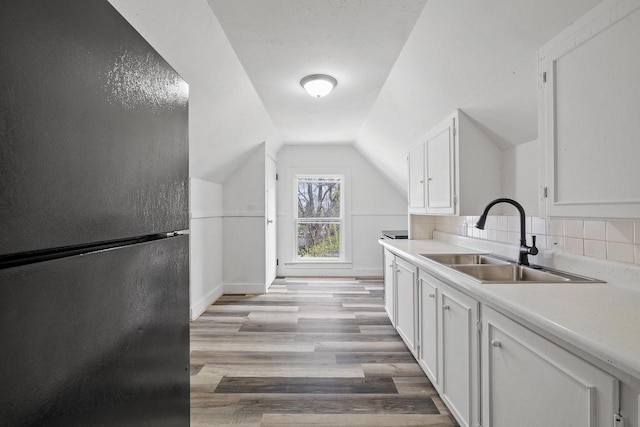kitchen with freestanding refrigerator, decorative backsplash, light countertops, white cabinets, and a sink