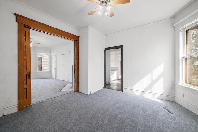 spare room with carpet floors, a ceiling fan, visible vents, and a healthy amount of sunlight