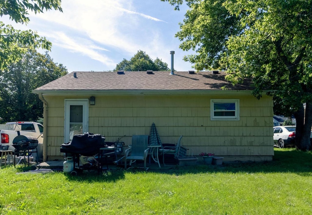 back of property with roof with shingles and a yard