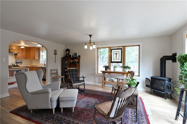 13195 Kavanaugh Rd, Cable, WI 54821 - living area featuring an inviting chandelier, a wood stove, arched walkways, light wood-style flooring, and baseboards