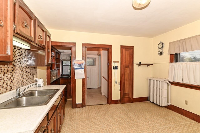 kitchen featuring backsplash, light countertops, a sink, radiator heating unit, and light floors