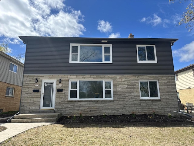 view of front of property with a chimney, a front lawn, and stone siding