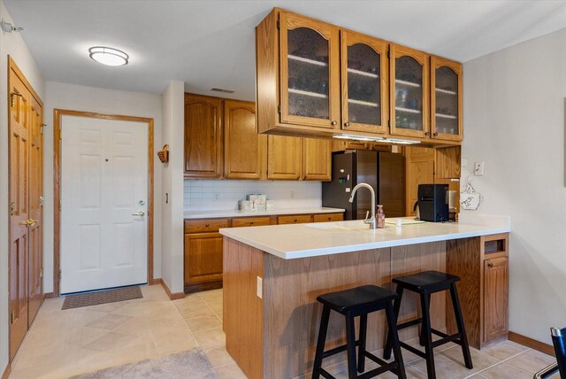 kitchen featuring freestanding refrigerator, a peninsula, brown cabinets, and a kitchen breakfast bar