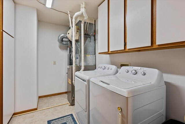 laundry area featuring washing machine and clothes dryer, baseboards, light tile patterned floors, and cabinet space