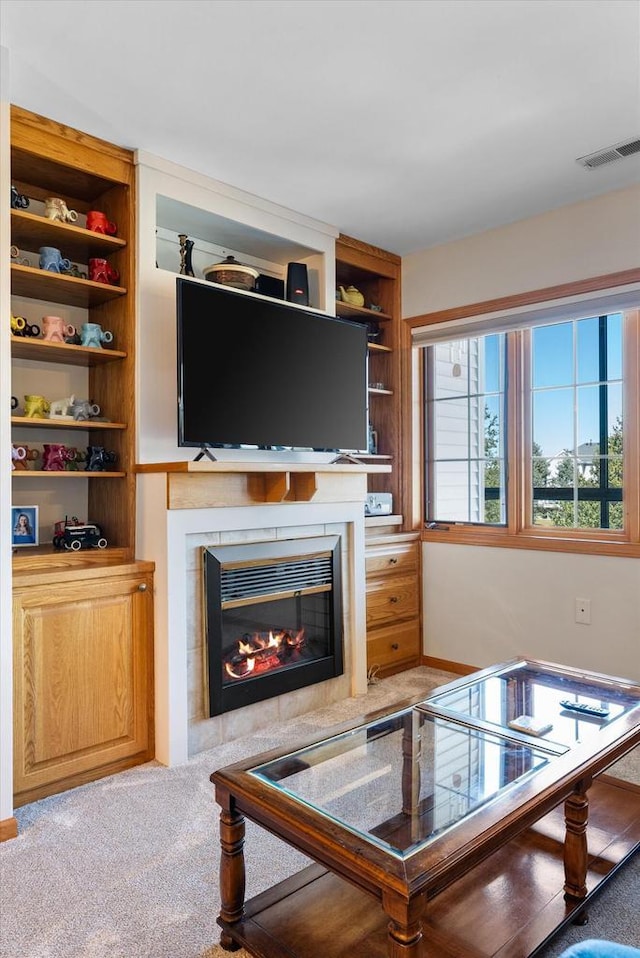 living room featuring visible vents, a glass covered fireplace, and light colored carpet