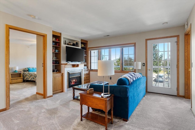 living room with a glass covered fireplace, baseboards, visible vents, and light colored carpet