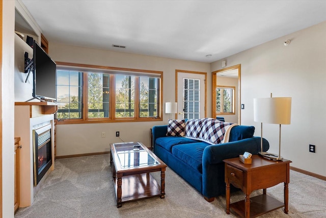 living room with a glass covered fireplace, baseboards, light carpet, and visible vents