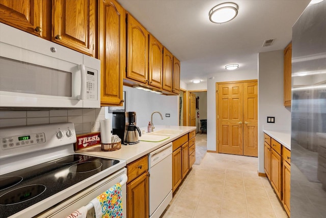 kitchen featuring a sink, white appliances, light countertops, brown cabinetry, and visible vents