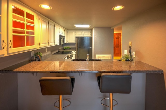 kitchen with black microwave, freestanding refrigerator, a peninsula, and stainless steel electric range