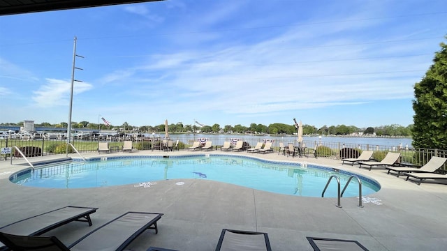 community pool with a water view, a patio area, and fence
