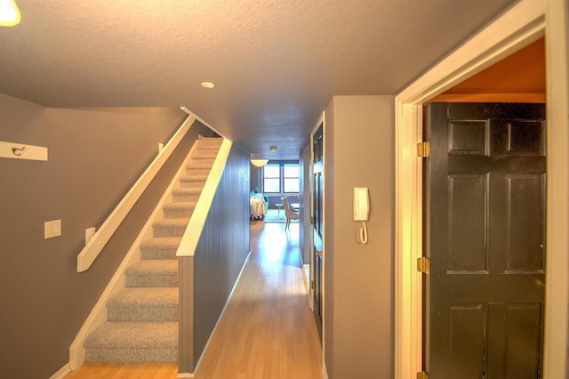 hall featuring a textured ceiling, stairs, recessed lighting, baseboards, and wood finished floors